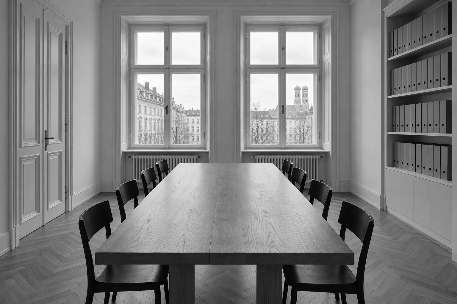 Besprechungsraum mit langem Eichentisch, schwarzen Holzstühlen und zwei hohen Fenstern zur Straße.